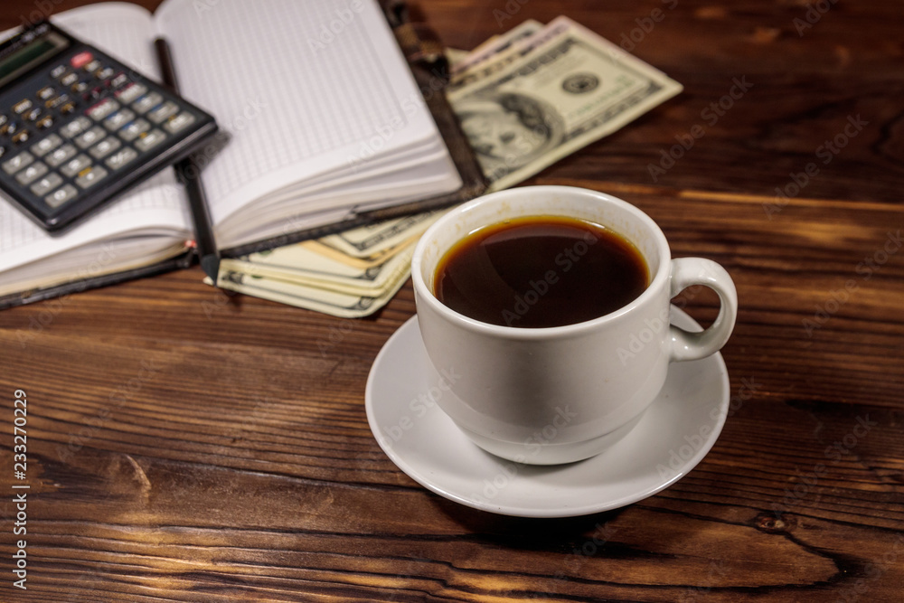 Cup of coffee and notepad with dollars, pencil and calculator on wooden desk. Financial concept Cup of coffee and notepad with dollars, pencil and calculator on wooden desk. Financial concept