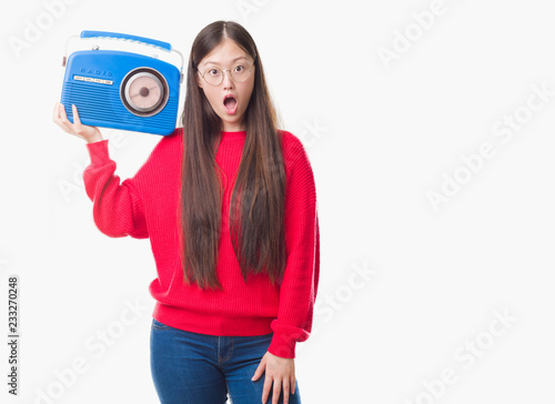 Young Chinese woman over isolated background holding vintage radio scared in shock with a surprise face, afraid and excited with fear expression