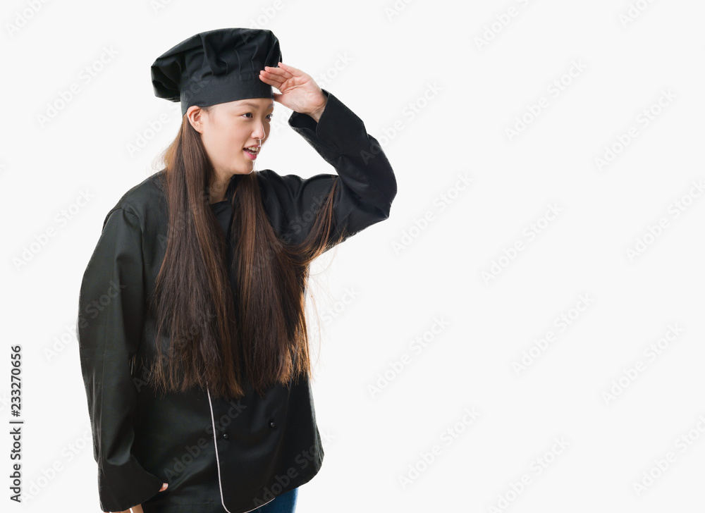 Young Chinese woman over isolated background wearing chef uniform very happy and smiling looking far away with hand over head. Searching concept. Young Chinese woman over isolated background wearing chef uniform very happy and smiling looking far away with hand over head. Searching concept.