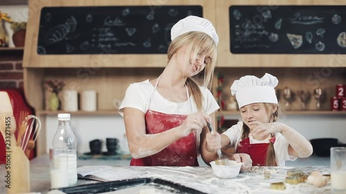 Mom and daughter in the same clothes have fun preparing a dough on a cozy kitchen. They mixing eggs in bowl at the kitchenl. Cooking, Mom and daughter concept photo