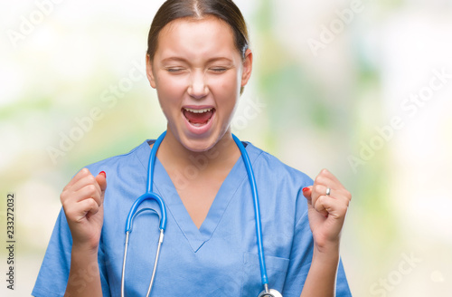 Young caucasian doctor woman wearing medical uniform over isolated background excited for success with arms raised celebrating victory smiling. Winner concept.