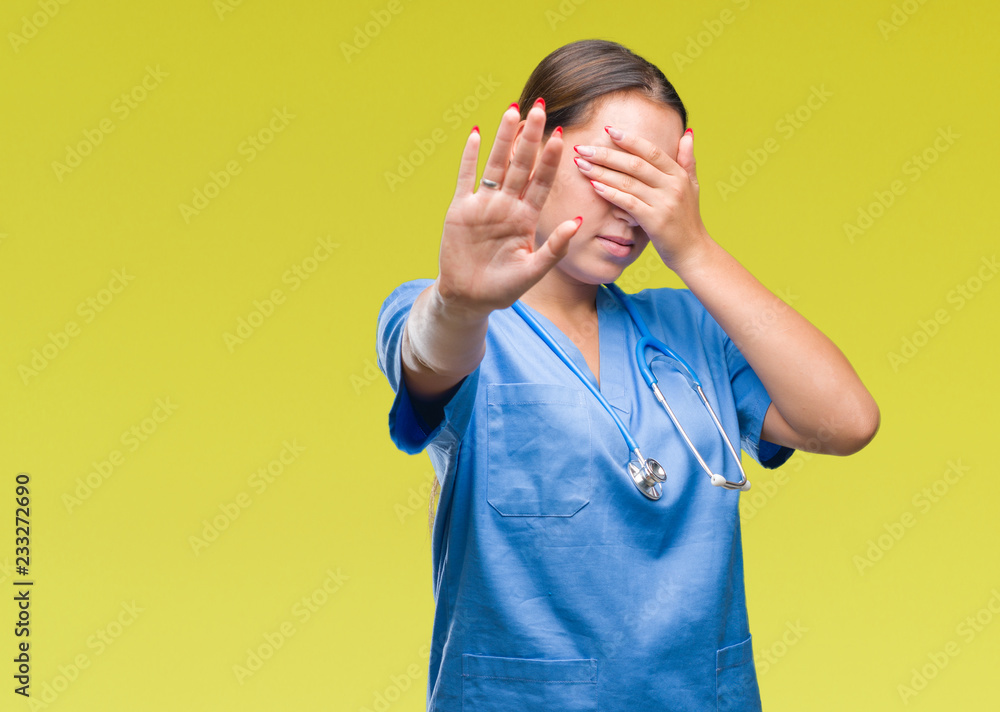 Young caucasian doctor woman wearing medical uniform over isolated background covering eyes with hands and doing stop gesture with sad and fear expression. Embarrassed and negative concept. Young caucasian doctor woman wearing medical uniform over isolated background covering eyes with hands and doing stop gesture with sad and fear expression. Embarrassed and negative concept.