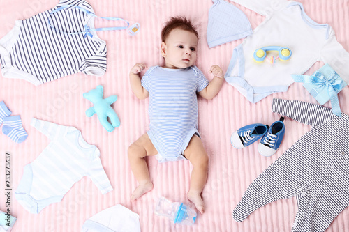 Cute baby with fashion clothes and toys lying on pink bed