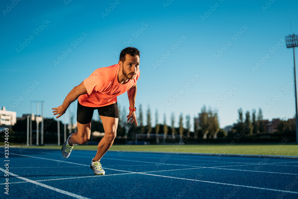 Fototapeta premium Young athlete man starting to run in a start position in a race. Start stride