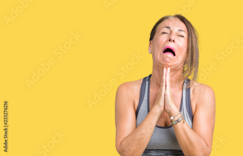 Obraz na plátně Beautiful middle age woman wearing sport clothes over isolated background begging and praying with hands together with hope expression on face very emotional and worried