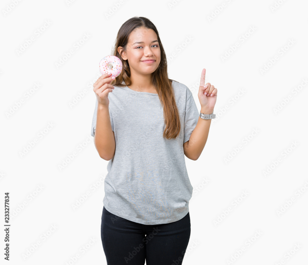 Young beautiful woman eating pink donut over isolated background surprised with an idea or question pointing finger with happy face, number one Young beautiful woman eating pink donut over isolated background surprised with an idea or question pointing finger with happy face, number one