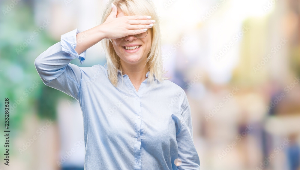 Young beautiful blonde business woman wearing glasses over isolated background smiling and laughing with hand on face covering eyes for surprise. Blind concept.