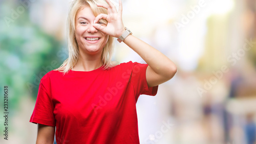 Young beautiful blonde woman wearing red t-shirt over isolated background doing ok gesture with hand smiling, eye looking through fingers with happy face.