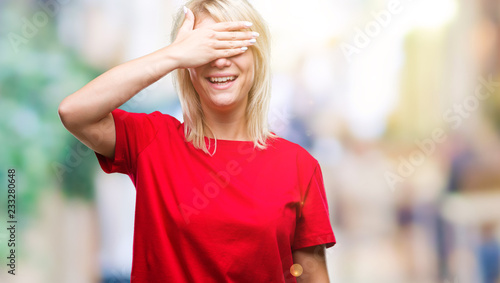 Fototapeta Naklejka Na Ścianę i Meble -  Young beautiful blonde woman wearing red t-shirt over isolated background smiling and laughing with hand on face covering eyes for surprise. Blind concept.