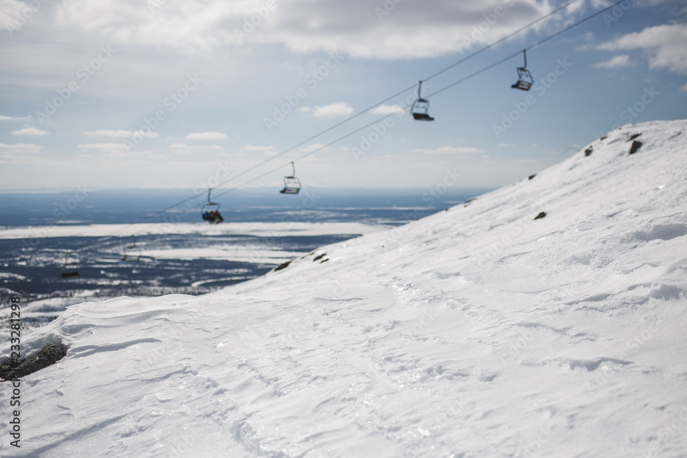 Obraz premium Shiny snow with blurred ski-lift cable car and mountain range. Copy space