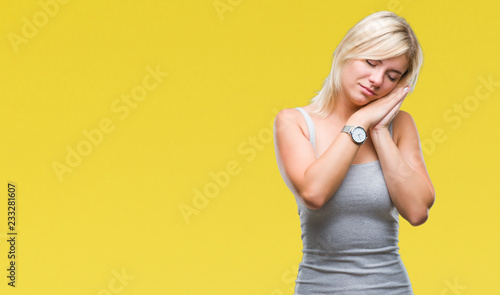 Young beautiful blonde woman over isolated background sleeping tired dreaming and posing with hands together while smiling with closed eyes. © Krakenimages.com