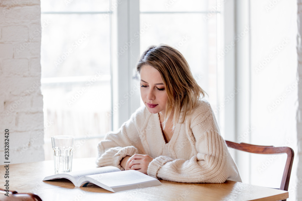 Tired caucasian girl in white sweater with book at kitchen. Home location Tired caucasian girl in white sweater with book at kitchen. Home location