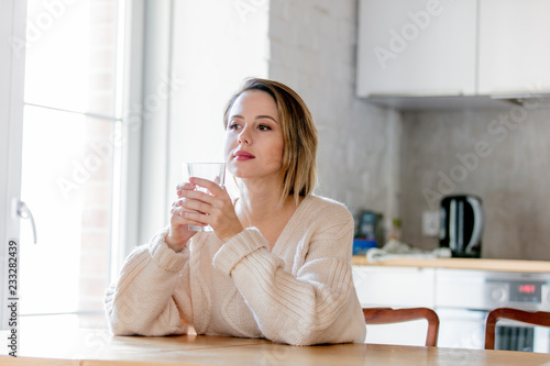 Young girl in sweater with glass of water at kitchen. Home interior