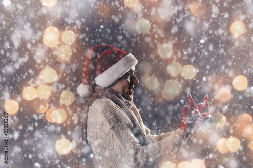 Christmas gift concept. Man in santa hat bring gift for you. Attractive man hold box. Christmas and new year holiday celebration. Man under snowflakes show fuck with middle finger