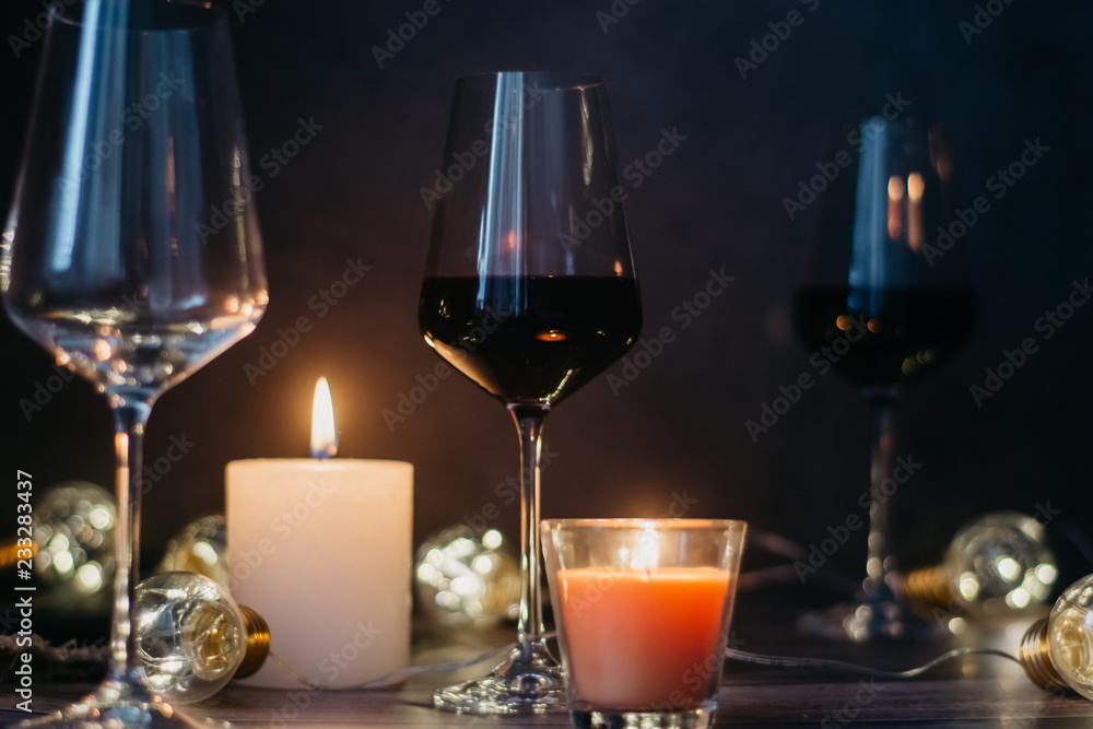 Holidays composition made of glass of red wine, candles and garlands on a dark background Holidays composition made of glass of red wine, candles and garlands on a dark background