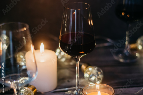 Holidays composition made of glass of red wine, candles and garlands on a dark background