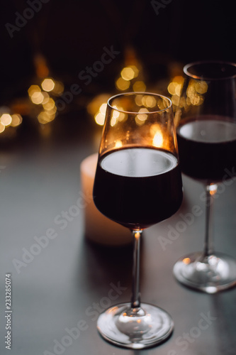Two glasses of wine  red standing on a dark table with candle and  garlands