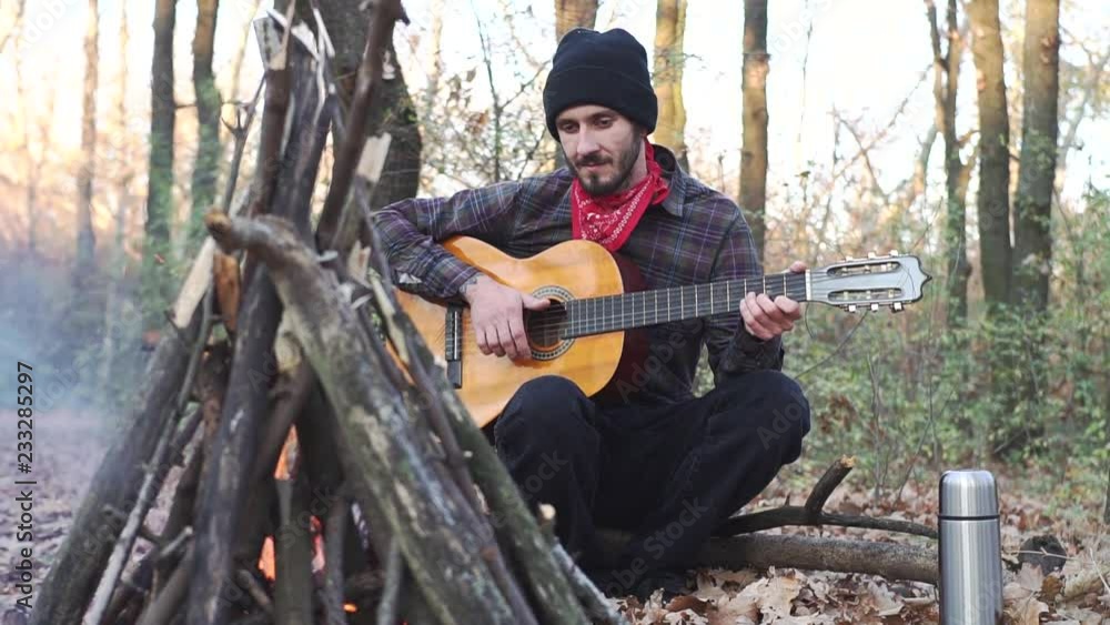 Young male traveler in the autumn forest play on guitar alone. Portrait of musician with acoustic guitar outdoors in the park Young male traveler in the autumn forest play on guitar alone. Portrait of musician with acoustic guitar outdoors in the park