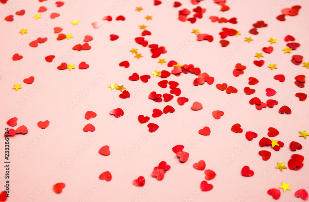 Defocused and blurred beautiful heart and stars shaped red confetti on pink background.