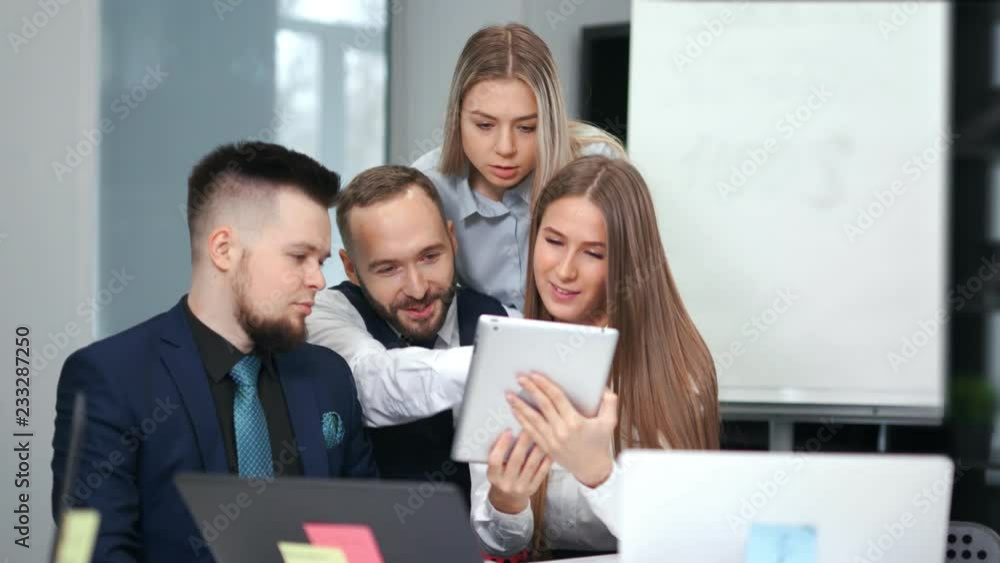 Group of young friendly business people having team meeting looking at screen tablet PC Group of young friendly business people having team meeting looking at screen tablet PC