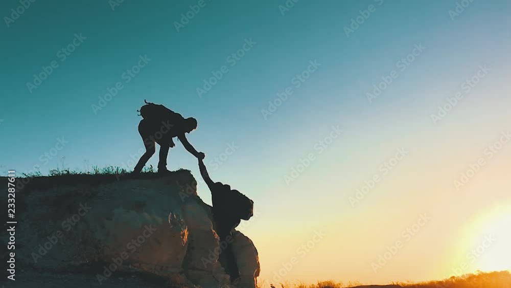 Silhouette of helping hand between two climber. two hikers on top of the mountain, a man helps a man to climb a sheer stone. couple hiking help each other silhouette in mountains with sunlight.