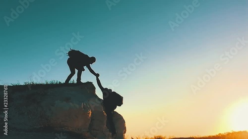 Silhouette of helping hand between two climber. two hikers on top of the mountain, a man helps a man to climb a sheer stone. couple hiking help each other silhouette in mountains with sunlight. photo