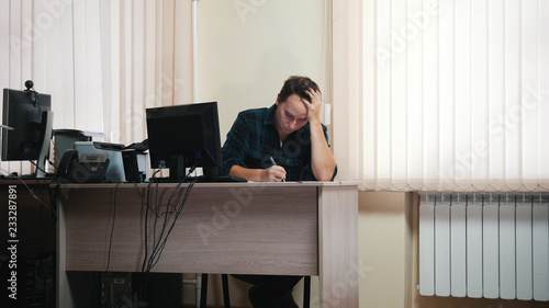 A man in office writing something and throws paper in trash