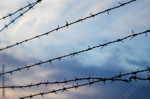 Silhouette of barbed wire fence against blurry cloudy sky in the evening. Focused on the foreground.