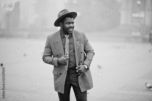 Stylish African American man model in gray jacket tie and red hat posed on street with fog. Black and white photo. photo