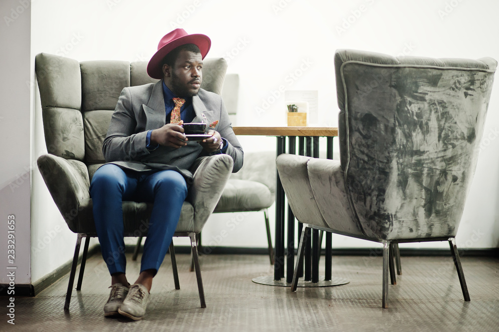 Stylish African American man model in gray jacket tie and red hat drink coffee at cafe.