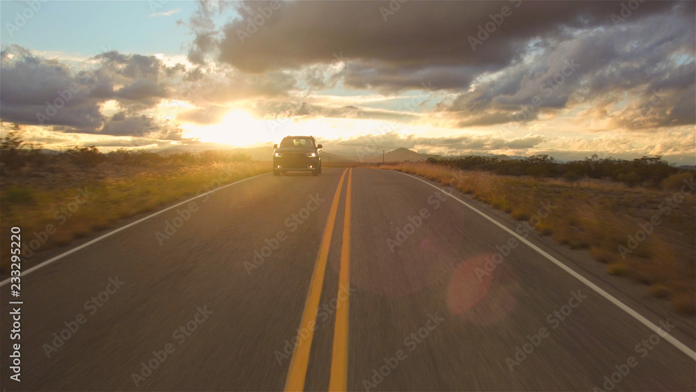 AERIAL: Black SUV car driving along the empty countryside road at golden sunset