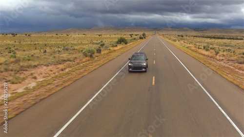 AERIAL: Black SUV car driving on wet empty countryside road in bad rainy weather