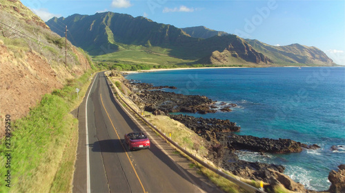 AERIAL: Couple in red convertible car driving along the beautiful coastal road