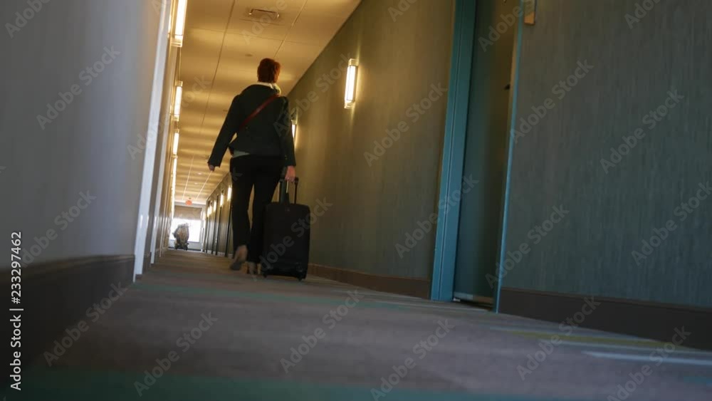 Woman walks down modern hotel hallway with luggage bag Woman walks down modern hotel hallway with luggage bag