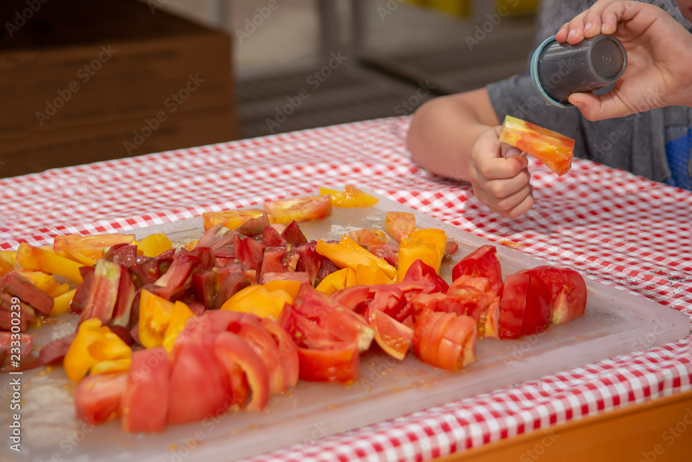 A kid enjoys tasting the free samples of cutup beefsteak tomatoes at the local farmers market.