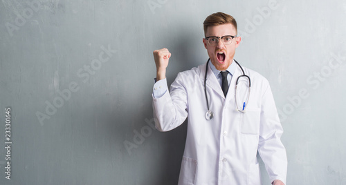 Young redhead doctor man over grey grunge wall annoyed and frustrated shouting with anger, crazy and yelling with raised hand, anger concept