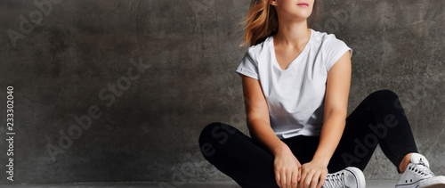 cropped shot of girl in jeans sitting on floor near grey wall photo