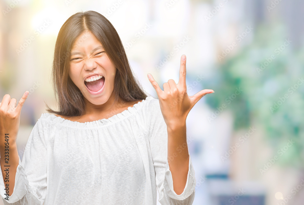 Young asian woman over isolated background shouting with crazy expression doing rock symbol with hands up. Music star. Heavy concept. Young asian woman over isolated background shouting with crazy expression doing rock symbol with hands up. Music star. Heavy concept.