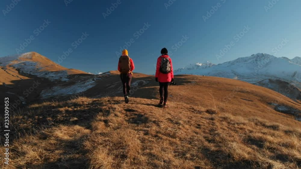 Aerial view of two traveling girls with backpacks and cameras stroll through the hills between epic rocks in the mountains. Girls photographers take pictures with their cameras at sunset Aerial view of two traveling girls with backpacks and cameras stroll through the hills between epic rocks in the mountains. Girls photographers take pictures with their cameras at sunset