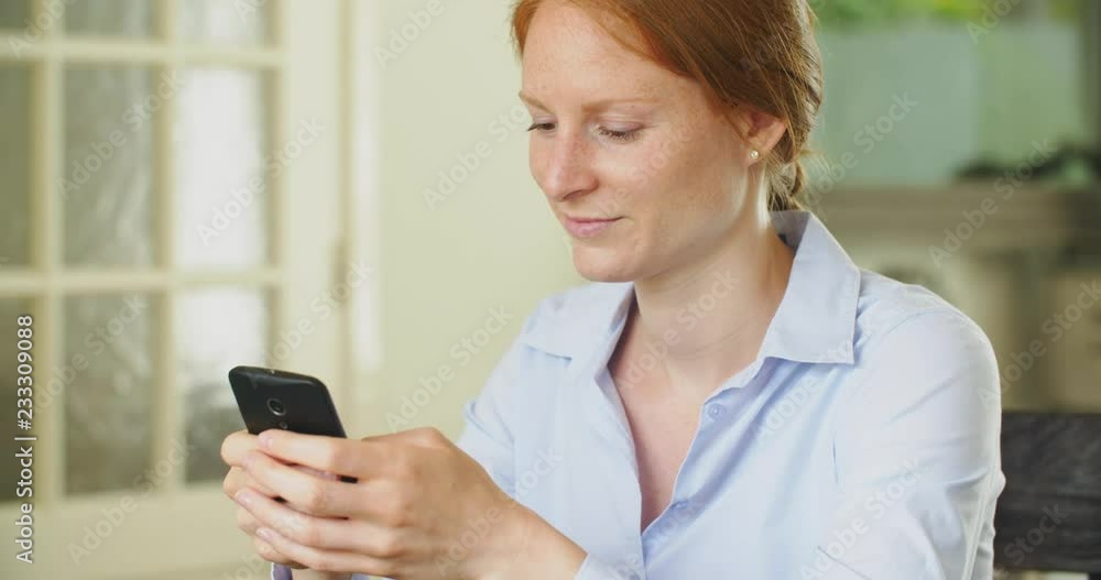 Young redhead businesswoman using a mobile phone at home. Young redhead businesswoman using a mobile phone at home.