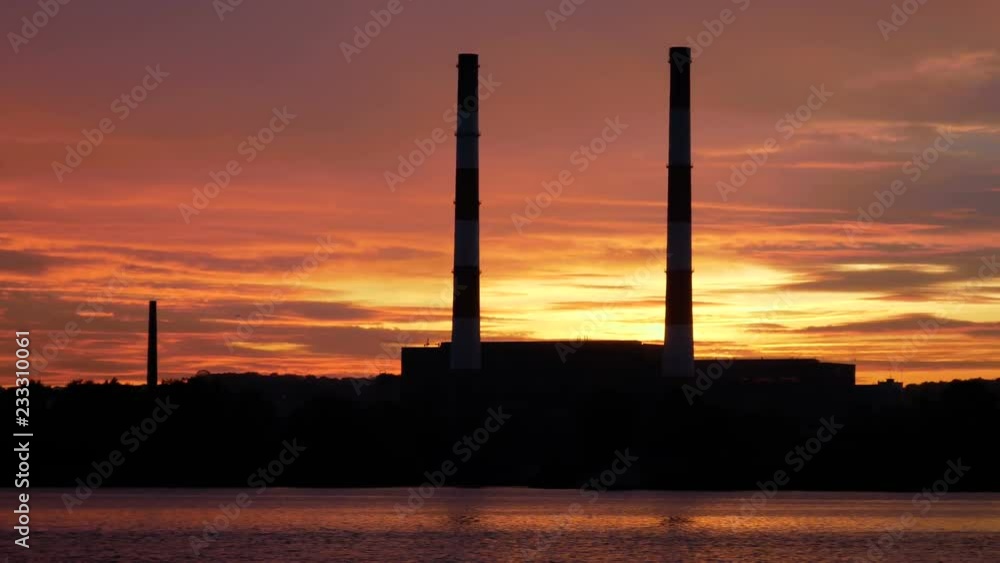 Incredible view of the evening city from the ship on the river in the background of the sunset. Silhouette of large pipes of the plant against the sky. Production by the river at the edge of the city Incredible view of the evening city from the ship on the river in the background of the sunset. Silhouette of large pipes of the plant against the sky. Production by the river at the edge of the city