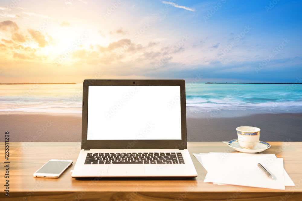 Mockup image of laptop with blank white screen,smart phone and document on wooden table at landscape early morning sunrise over the sea the horizon background.
