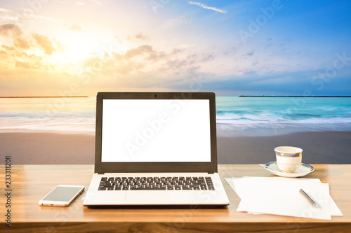Mockup image of laptop with blank white screen,smart phone and document on wooden table at landscape early morning sunrise over the sea the horizon background.