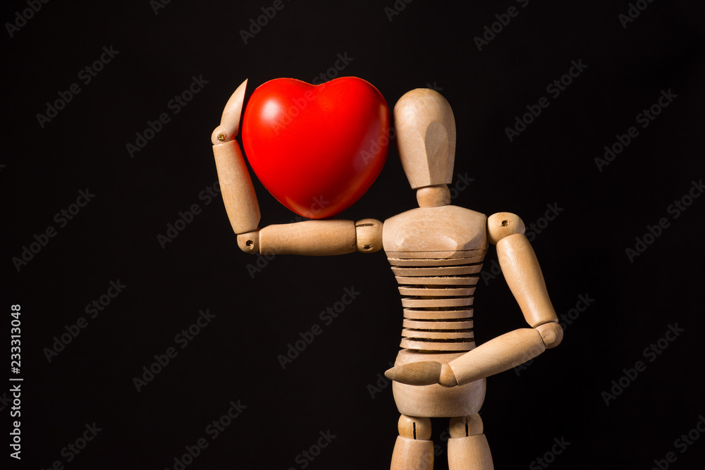 Wooden puppet with a red heart in his hands on a black background