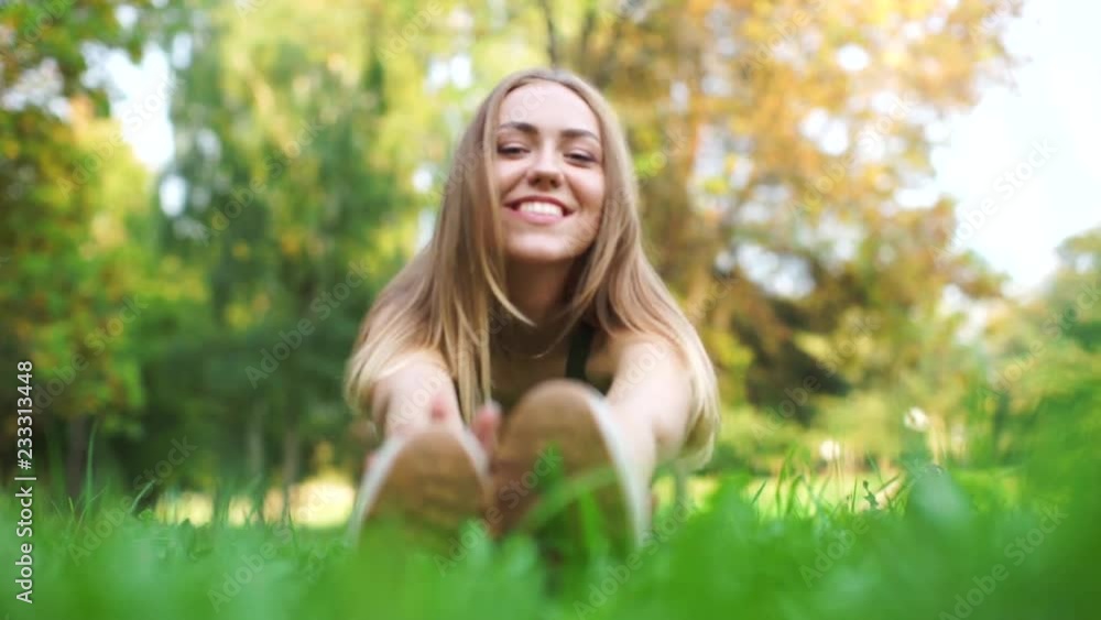 Beautiful girl sitting on the grass and stretches to his feet. Athlete doing stretching. The blonde looks at the camera and smiles. Cute girl goes in for sports in the nature. Beautiful girl sitting on the grass and stretches to his feet. Athlete doing stretching. The blonde looks at the camera and smiles. Cute girl goes in for sports in the nature.