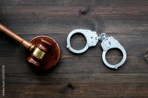 Arrest concept. Metal handcuffs near judge gavel on dark wooden background top view copy space