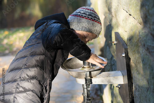 boy is drinking water from drinking fountain in a park; cool amd sunny fall day. 