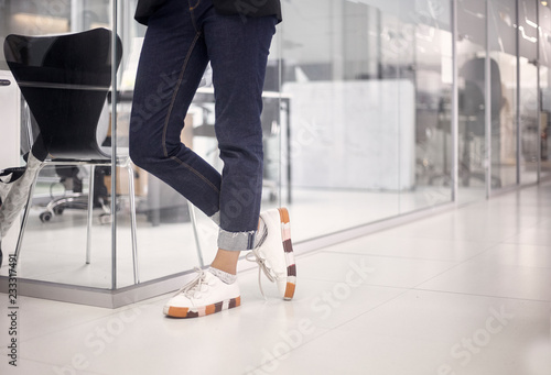 close-up shot of woman wearing jeans and sneakers  smart casual  in white modern office floor  interior. low angle view.