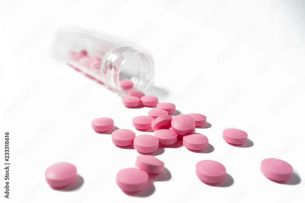 Several large bright pink tablets poured from a glass jar on white background Several large bright pink tablets poured from a glass jar on white background