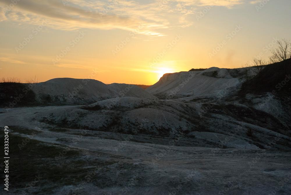 A blue sunset sky with white clouds and white Cretaceous deposits. Extraction of chalk. An open chalk rock quarry mine. Industrial extraction of chalk and clay by mining. Sunset lighting.